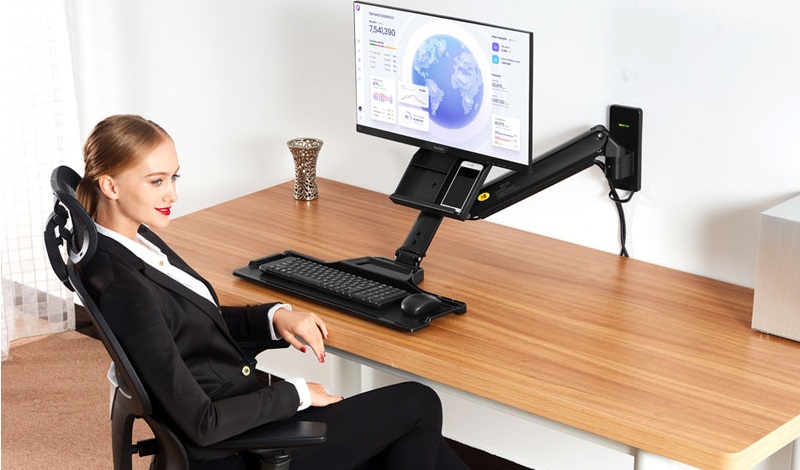 Cô gài ngồi trước bàn có giá treo màn hình PC với thiết kế gắn tường phù hợp nhu cầu sử dụng văn phòng, gia đình